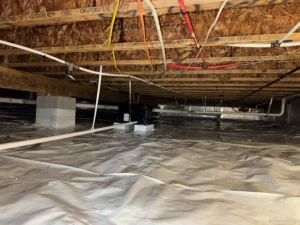 A fully encapsulated crawlspace in Chapel Hill, NC, featuring a reflective plastic liner on the ground, white PVC pipes, and electrical wiring secured to wooden beams, indicating a completed moisture control setup.