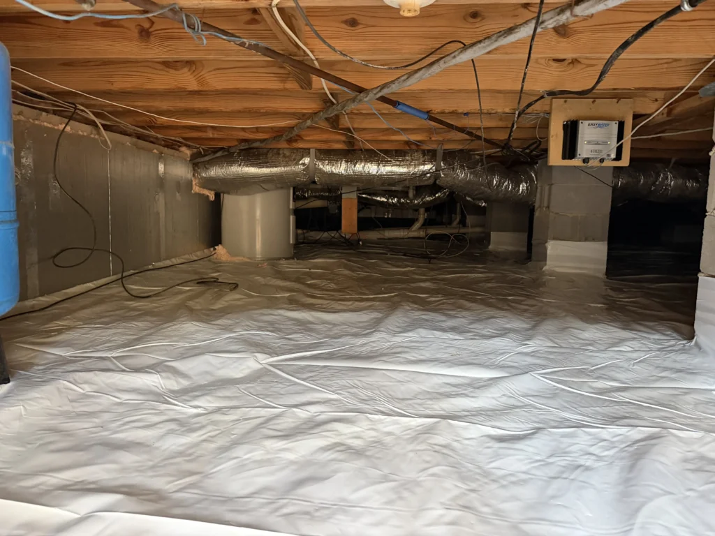 A clean, dry crawl space fully encapsulated with a white vapor barrier covering the ground and foundation walls.