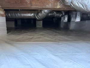 White crawlspace vapor barrier installed across the ground and foundation walls to help control moisture beneath a 100-year-old home.